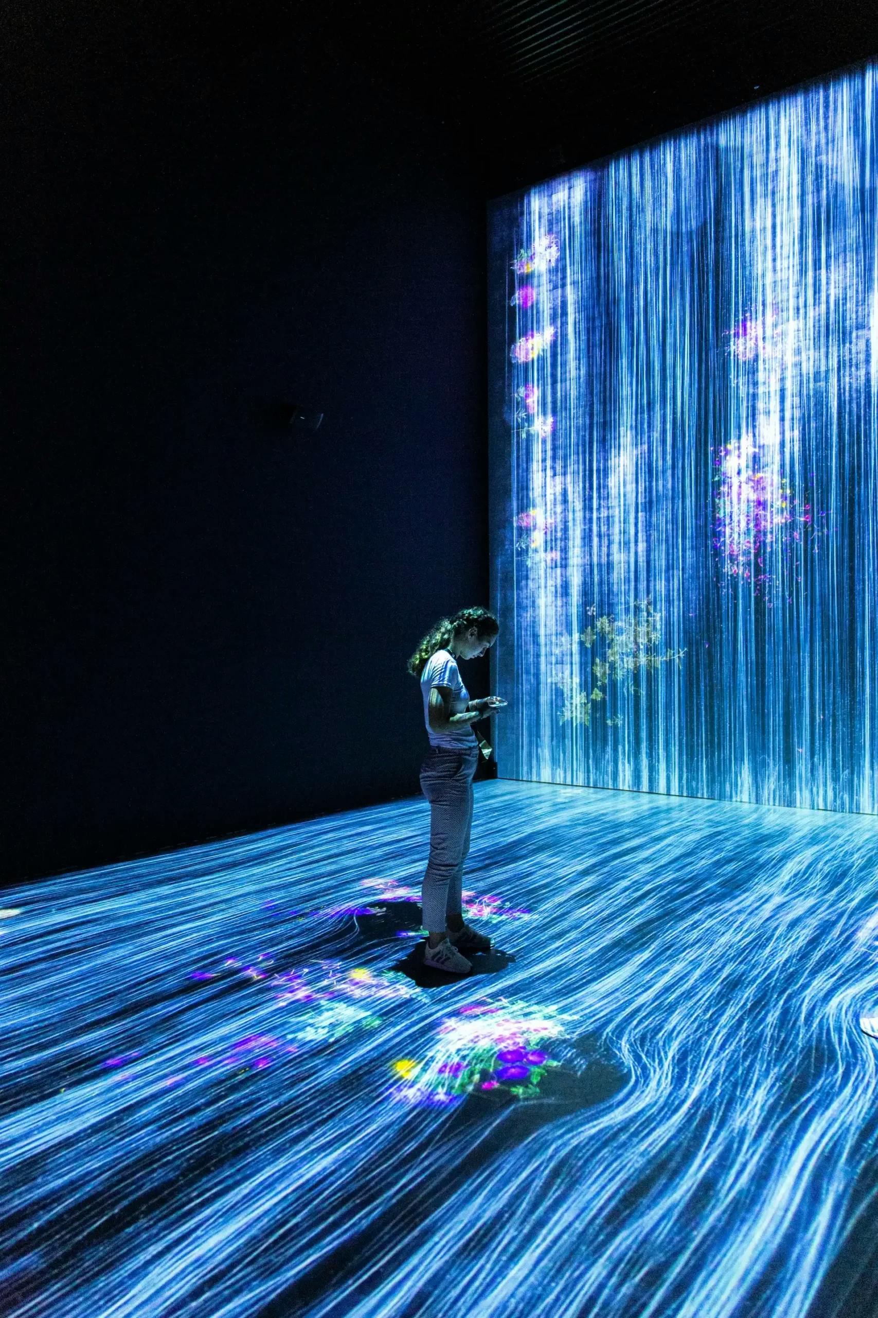 Person experiencing an interactive digital art installation with vibrant light patterns on the walls and floor
